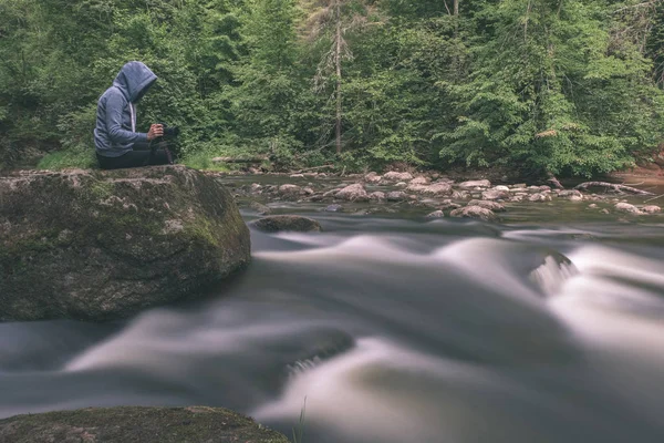 身穿蓝色连帽的人坐在岩石上 长曝光岩石山河 — 图库照片