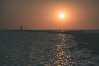 dalgakıran deniz günbatımı insanlar tarafından - vintage bir retro görünüm ile sonunda kırmızı deniz feneri ile
