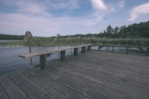 Wooden and composite material foot bridge over water in green summer forest surroundings with lake