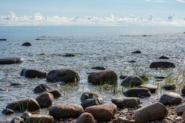 deniz suyu Letonya mavi gökyüzü altında büyük sert kayalarda