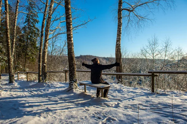 man welcoming fosun rising in heavy snow covered foirst light, sitting on wooden bench. est. first rays of light shining on frost iced tree branches and coloring vast landscape