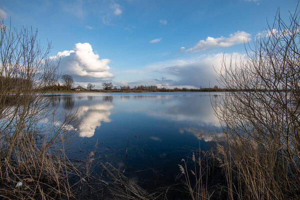 calm lake in bright sun light with reflections of clouds and trees and blue sky. summer in countryside