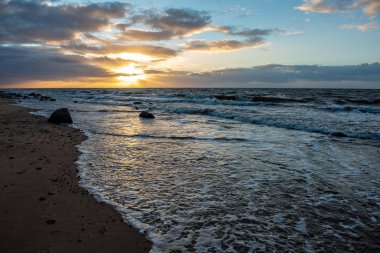 Deniz plaj kayalar ve fırtınalı su üzerinde dramatik günbatımı