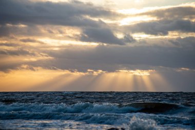 Deniz plaj kayalar ve fırtınalı su üzerinde dramatik günbatımı