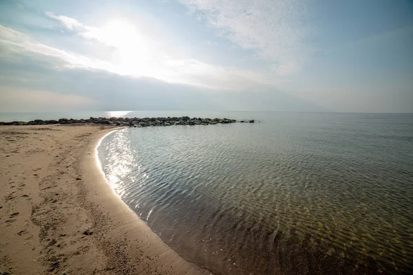 Calm sea beach in summer with large rocks and wooden poles from — Stock Photo, Image