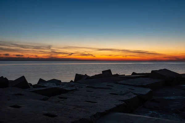 Dramatic sunset over sea beach with rocks and stormy water — Stock Photo, Image