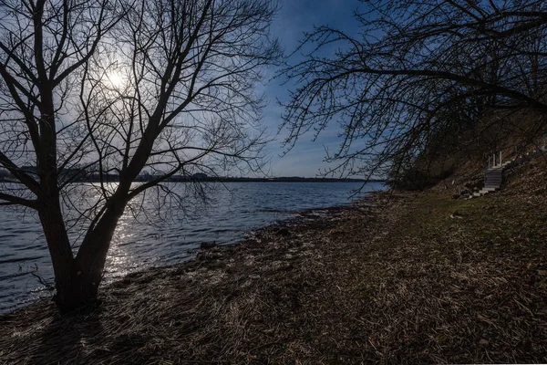 Naakte Boomtakken Kleuren Van Zonsondergang Tegen Kalme Glanzende Water Bezinningen — Stockfoto