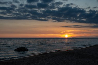 koyu mavi su ve dramatik kontrastlı bulutlar ile sakin deniz Plajı üzerinde renkli günbatımı. suda kayalar
