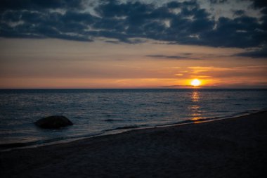 koyu mavi su ve dramatik kontrastlı bulutlar ile sakin deniz Plajı üzerinde renkli günbatımı. suda kayalar