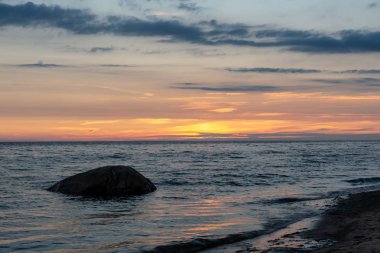 koyu mavi su ve dramatik kontrastlı bulutlar ile sakin deniz Plajı üzerinde renkli günbatımı. suda kayalar