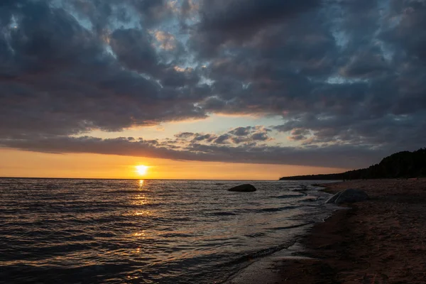 五颜六色的日落在平静的海滩与深蓝色的水和戏剧性的对比云 水中的岩石 — 图库照片