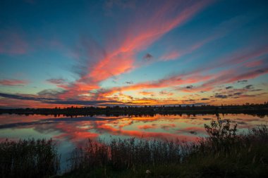 yansımaları ile mavi gökyüzünde yeşil çim çayır ve beyaz bulutlar ile göl kenarında güzel gün batımı