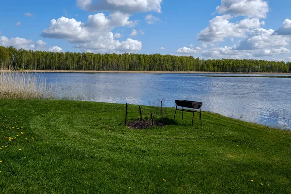 recreation camping area by the blue lake in sunny summer day on the shore of water body with trees, green meadow with dandelions and boats on the shore