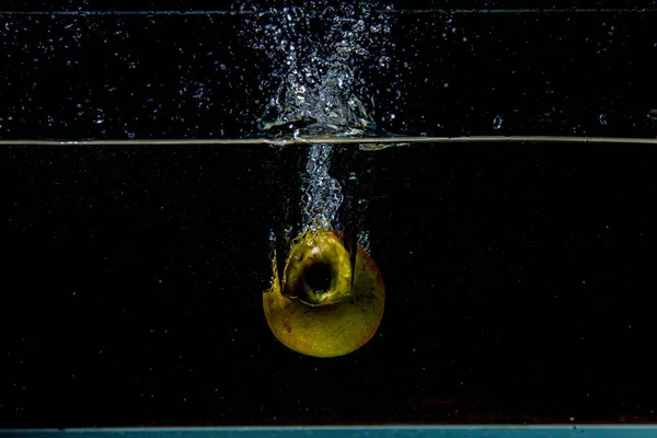 Mela che cade in acqua scura con spruzzi — Foto Stock