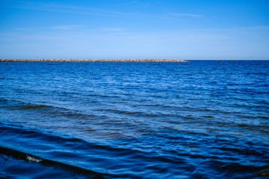 yaz gökyüzü altında mavi su ile kayalık sahil plaj