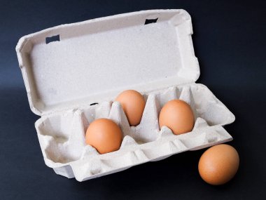 Geri dönüştürülmüş kağıdın yumurta panellerinin üzerinde koyu arkaplanda yumurtalar var. Çevre dostu ambalaj.