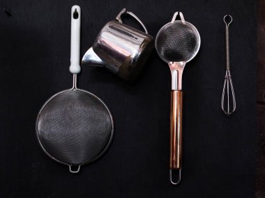 Ahşap arka planda kevgir ve çırpıcılı mutfak aletleri.