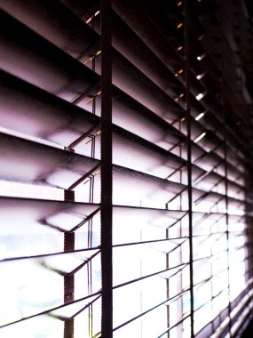 Güneş ışığı, oturma odasındaki kahverengi ahşap panjurlarla pencereyi aydınlatıyor..