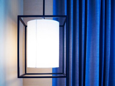 Tavandan sarkan siyah çelik lamba, arka plan boşluğuyla dekore edilmiş mavi perde..