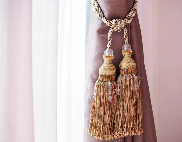 Brown curtain with rope tassel and sheer curtains.