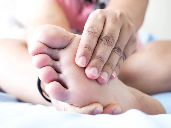 Yatakta oturan Asyalı kadın ayak ağrısı çekiyor. Acıyı hafifletmek için el masajı yap ve ayak kaslarını gevşet. Plantar Fasciitis hastalığı..