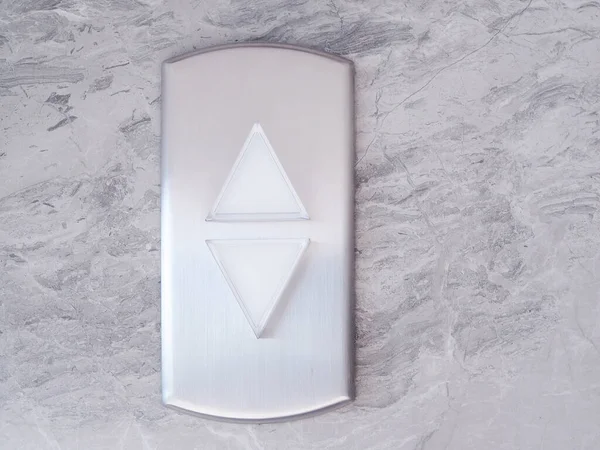 Elevator with lift silver button triangle up and down on marble pattern wall.