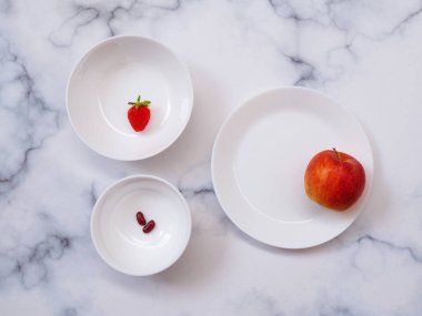 Seramik tabağın üst görüntüsü ve kırmızı meyve diyeti olan beyaz kase mermer masa arkasında izole edilmiş sağlıklı yiyecekler..