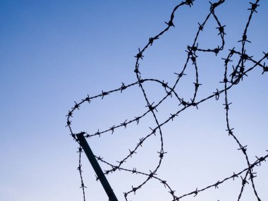 Gün batımında metal tel örgüler ve dikenli tel örgüler üzerinde siluet.
