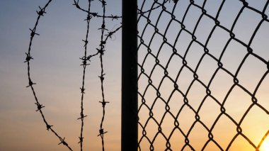 Gün batımında karanlık gökyüzü ve dikenli tel örgü silueti.