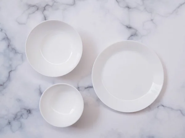 Top view of white ceramic plate or round dish, bowl and crockery set on mable table.