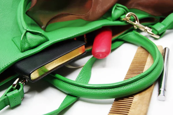 Things from lady purse isolated on white background. Cosmetics and women\'s accessories fell out of green handbag. Notebook, wooden comb, lipstick, brown scarf