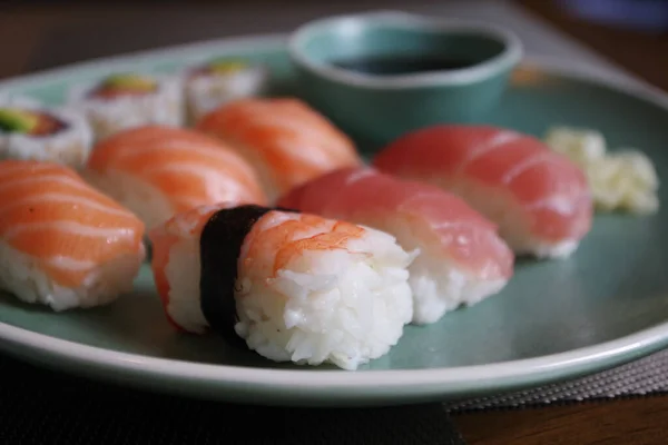 Japanese sushi food. Sushi set on green plate served with ginger and soy sauce. Sushi rolls, salmon nigiri, shrimp nigiri, tuna nigiri