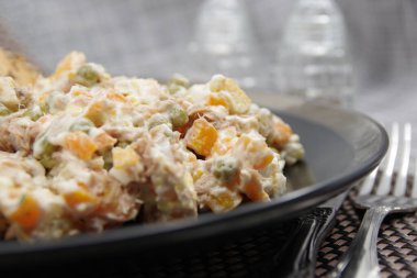 Siyah tabakta ton balığı salatası. İçindekiler: ton balığı, havuç, yumurta, soğan, konserve bezelye, kızarmış ekmek, mayonez.