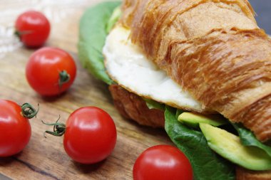 Tahta tepside kruvasan doldurulmuş yumurta ve avokado.