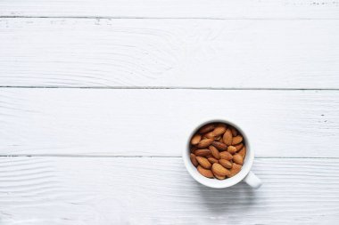 Beyaz kahve fincanındaki kavrulmuş badem manzarası beyaz ahşap arka plana yerleştirilmiş, uzay konseptini kopyala.