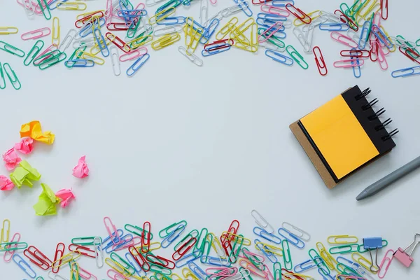 Notepad and colorful paper clips poured on white background.
