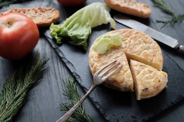 Patates omletinin bir kısmı kayrak ve siyah arkaplanda.