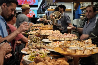 SAN SEBASTIAN, İSPAN - 17 Temmuz 2019 'da İspanya' nın San Sebastian kentindeki San Sebastian kentindeki bir barın barından pintxoları izleyip yiyen turistler.