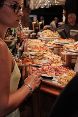 SAN SEBASTIAN, İSPAN - 17 Temmuz 2019 'da İspanya' nın San Sebastian kentindeki San Sebastian kentindeki bir barın barından pintxoları izleyip yiyen turistler.
