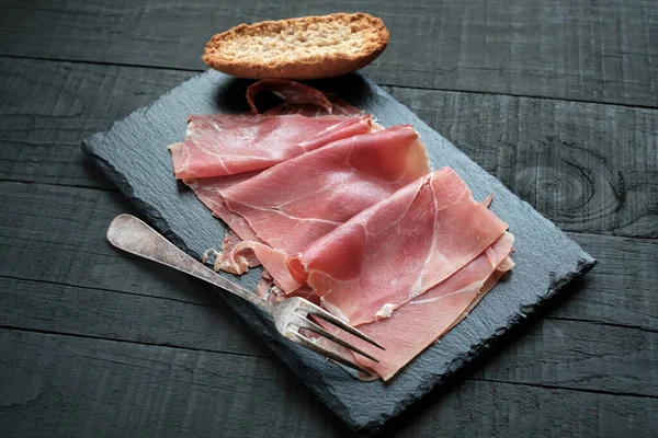 İspanyol jambonu dilimleri tahtada ve siyah masada.