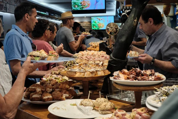SAN SEBASTIAN, İSPAN - 17 Temmuz 2019 'da İspanya' nın San Sebastian kentindeki San Sebastian kentindeki bir barın barından pintxoları izleyip yiyen turistler.