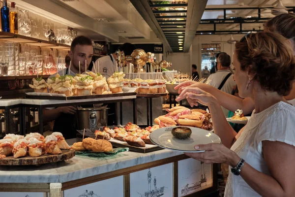 SAN SEBASTIAN, İSPAN - 17 Temmuz 2019 'da İspanya' nın San Sebastian kentindeki San Sebastian kentindeki bir barın barından pintxoları izleyip yiyen turistler.