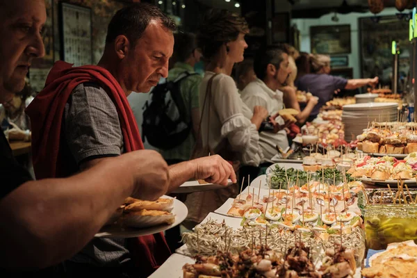 SAN SEBASTIAN, İSPAN - 17 Temmuz 2019 'da İspanya' nın San Sebastian kentindeki San Sebastian kentindeki bir barın barından pintxoları izleyip yiyen turistler.