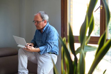 Evde dizüstü bilgisayarla sıradan çalışan olgun bir adam.