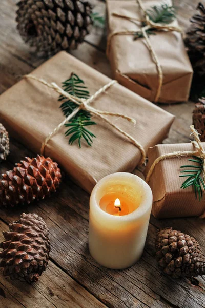 Gift packages wrapped with kraft paper, and surrounded by pine cones and a candle