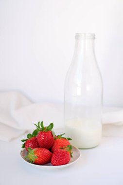 Tatlı tabağında iştah açıcı çilekler ve beyaz arka planda bir şişe taze süt.