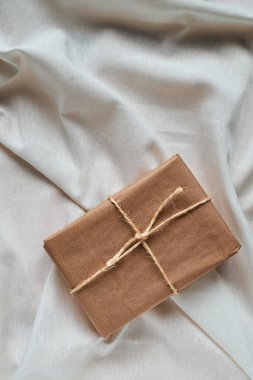 Kırışık beyaz kumaş üzerine sarılı jüt kağıt hediye paketi