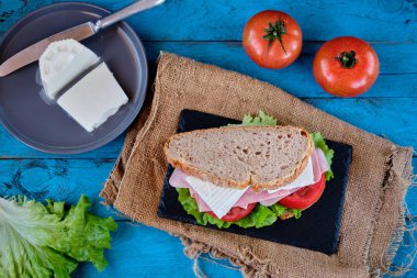 Mavi masada domates ve marullu jambonlu peynirli sandviç.
