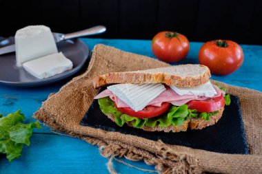 Mavi masada domates ve marullu jambonlu peynirli sandviç.