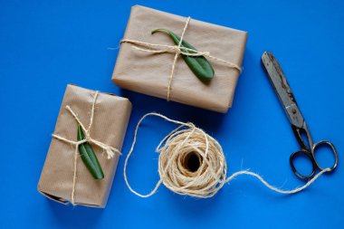 Kraft kağıdında hediye paketleri, makas ve halat mavi arkaplanda